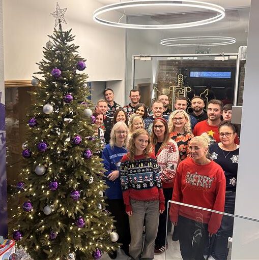 The Ramsbottom team wearing thier Christmas jumpers and standing next to the Christmas tree smiling 